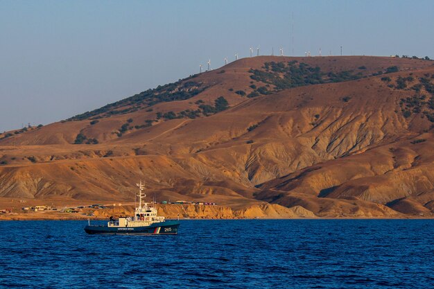 Mała łódź żaglowa na błękitnym morzu o zachodzie słońca z widokiem na góry.