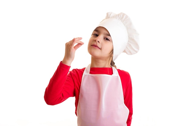 Mała miła dziewczyna ubrana w czerwoną koszulę z białym fartuchem i czapką kuchenki w studio