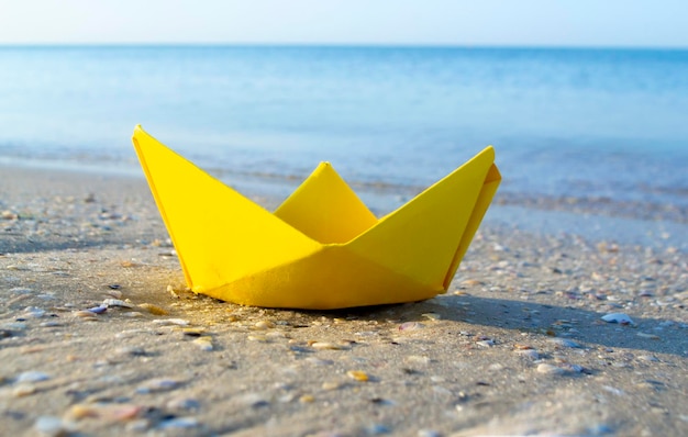 Mała papierowa żółta łódka na piasku w pobliżu wody na tle fal morskich