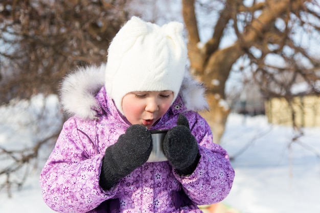 Mała piękna dziewczyna pije herbaty na ulicie w zimie.