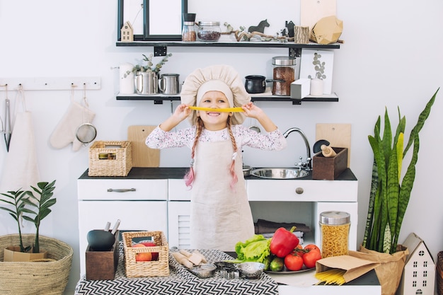 Mała piękna dziewczynka gotuje w kuchni z różnymi warzywami i spaghetti