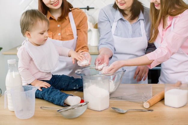 Zdjęcie mała piękna dziewczynka z matką, ciocią i babcią trzyma mąkę w ich rękach i robi ciastu wpólnie w domu. koncepcja pieczenia szefa kuchni dla niemowląt.