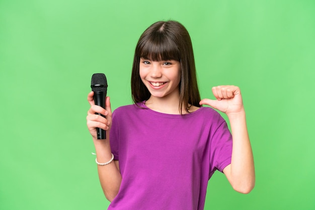 Mała piosenkarka podnosi mikrofon na odosobnionym tle, dumna i zadowolona z siebie