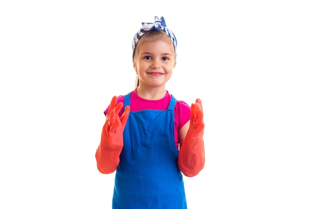 Mała pozytywna dziewczyna z kucykiem ubrana w różową koszulę i niebieski fartuch z czerwonymi rękawiczkami w studio