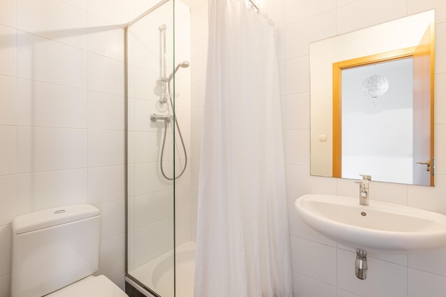 Mała, prosta, jasna łazienka z kabiną prysznicową otoczoną szklaną przegrodą i kwadratowym lustrem z ekranem