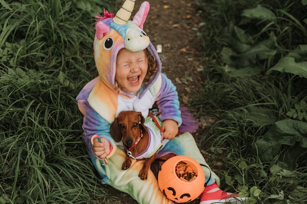 Mała Roześmiana Dziewczynka I Pies W Kostiumach Na Halloween Z Dyniowym Koszem Na Słodycze Na świeżym Powietrzu