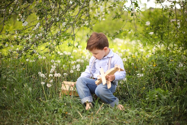 Mała śliczna blond chłopiec bawić się z drewnianym samolotem w lato parku na trawie na słonecznym dniu