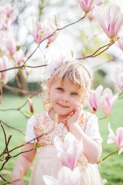 Mała śliczna blondynka 3 lata bawi się w parku w pobliżu kwitnącej magnolii. Wiosna.