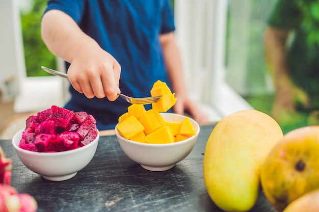 Mała śliczna chłopiec je mango na tarasie