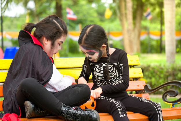 Mała śliczna Dziewczyna Asia W Halloweenowym Kostiumu Dzieli Cukierki I Cukierki Podczas Gdy Siedzący Przy ławką Na Boisku.