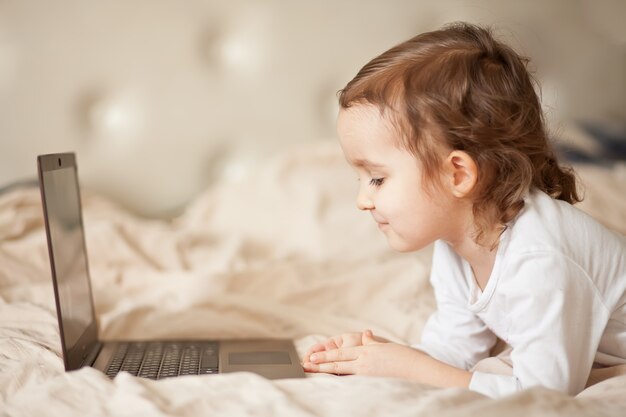 Mała śliczna dziewczyna kłama na łóżku i używa cyfrowego laptop