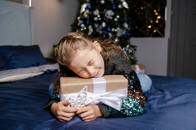 Mała śliczna dziewczyna otrzymała prezent świąteczny. Ciesz się otrzymywaniem prezentów. Dziecko podekscytowane rozpakowywaniem prezentu. Koncepcja Bożego Narodzenia, wakacji i dzieciństwa