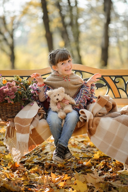 Mała śliczna Dziewczyna Siedzi Na ławce W Jesień Parku. Dziewczyna Schroniła Się, żeby Się Ogrzać. Jesienny Czas.