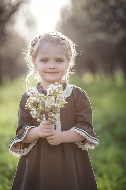 Mała śliczna Dziewczyna W Sukience W Ogrodzie Kwiat. Cute Dziewczynka 3-4 Lat Gospodarstwa Kwiaty Nad Naturą. Portret Wiosny. Aromatyczny Kwiat I Koncepcja Retro Vintage.