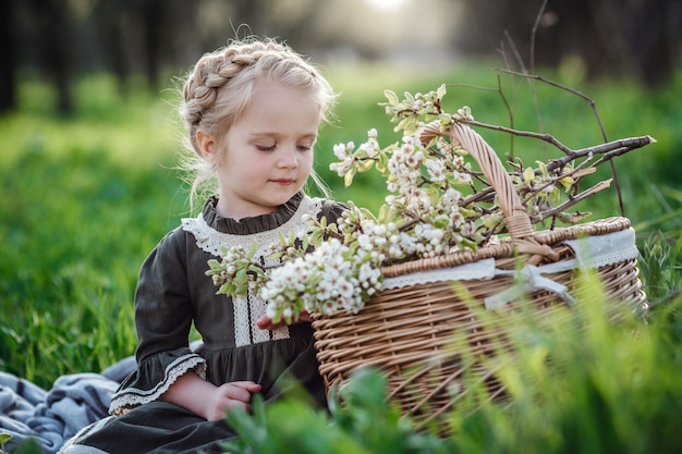 Mała śliczna dziewczyna w sukience w ogrodzie kwiat. Cute dziewczynka 3-4 lat gospodarstwa kwiaty nad naturą. Portret wiosny. Aromatyczny kwiat i koncepcja retro vintage.