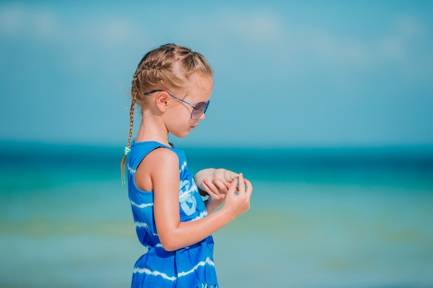 Mała śliczna dziewczyna z seashell w rękach przy tropikalną plażą.