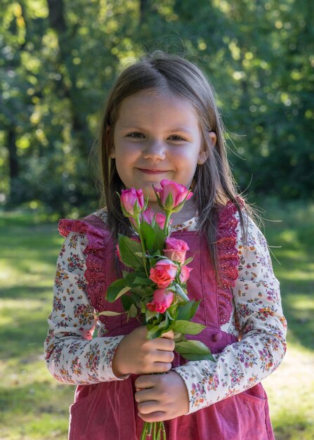 Zdjęcie mała śliczna dziewczynka w różowej sukience trzyma róże w dłoniach i patrzy na nie wesoło