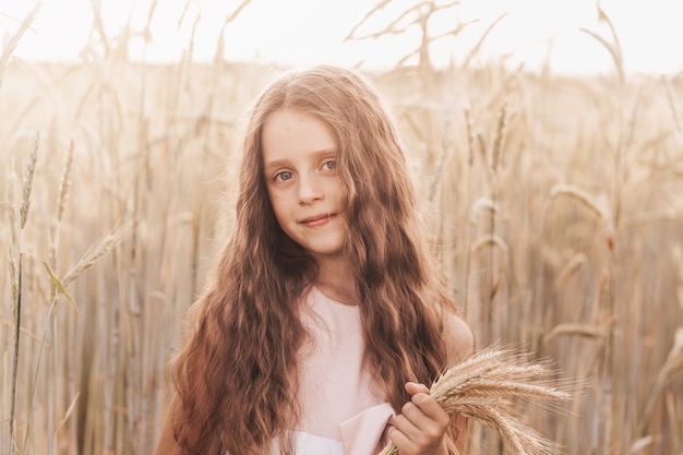 Mała słodka dziewczyna z długimi włosami trzyma kłoski pszenicy na polu w lecie. Lato. Koncepcja zbiorów