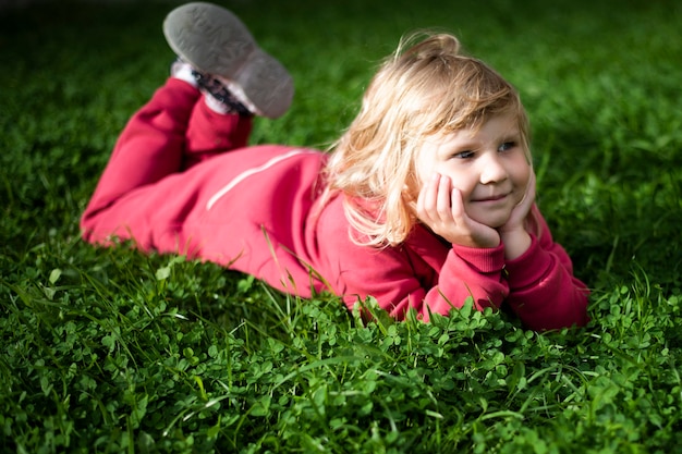 Mała słodka dziewczynka 5-letnia blondynka w czerwonych ubraniach na trawie