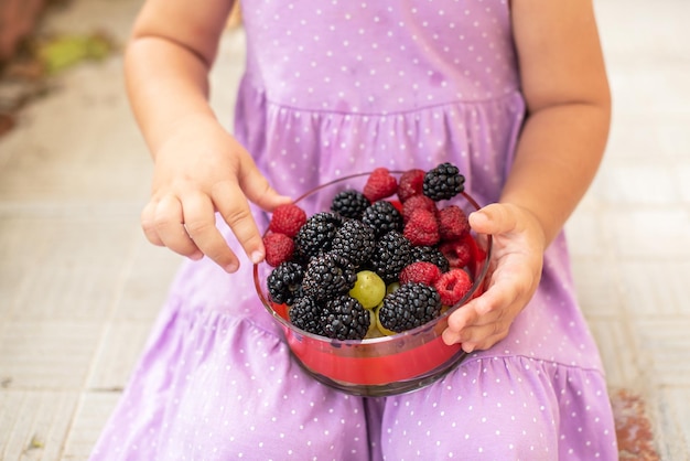 Zdjęcie mała słodka dziewczynka chętnie je owoce maliny i jeżyny pyszne i zdrowe jedzenie dla dzieci