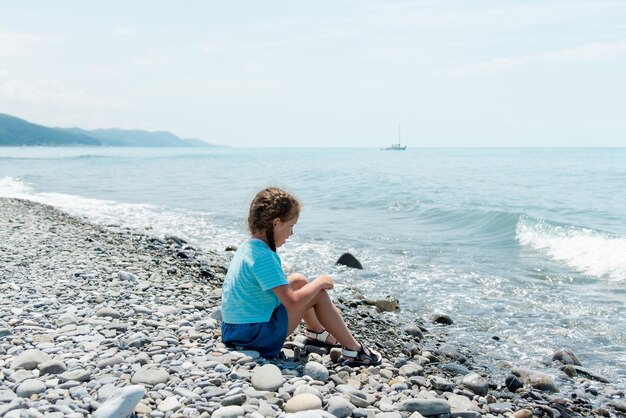 Mała słodka dziewczynka siedzi na kamienistej plaży i bawi się kamykami