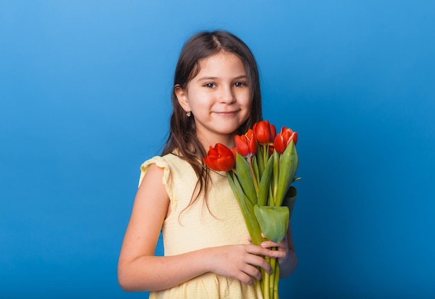 Mała słodka dziewczynka trzyma bukiet tulipanów na niebieskim tle Szczęśliwy dzień kobiet Miejsce na tekst Żywe emocje 8 marca