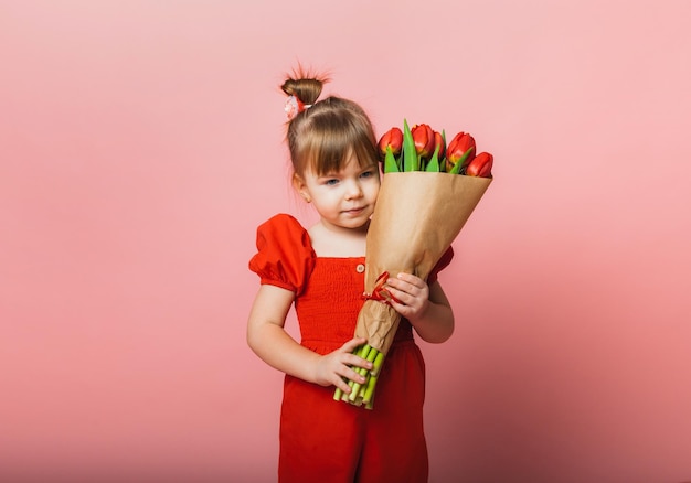 Mała słodka dziewczynka trzyma bukiet tulipanów w opakowaniu rzemieślniczym na różowym tle Szczęśliwy dzień kobiet Miejsce na tekst