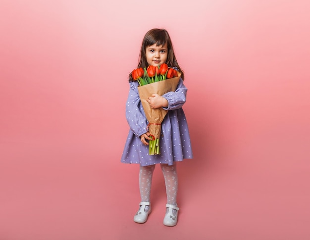 Mała słodka dziewczynka trzyma bukiet tulipanów w opakowaniu rzemieślniczym na różowym tle Szczęśliwy dzień kobiet Miejsce na tekst