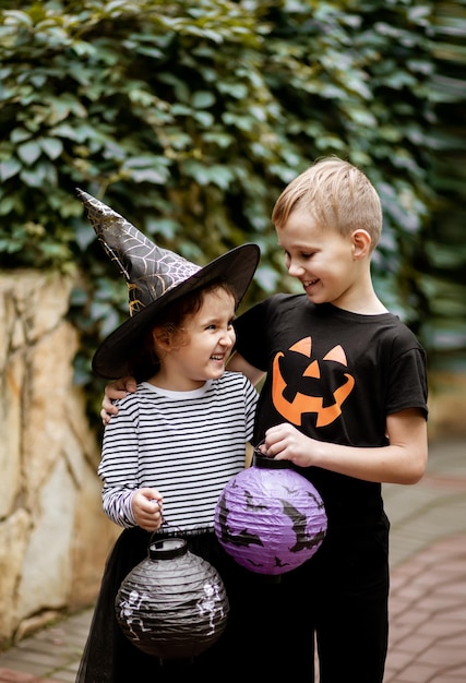 Zdjęcie mała słodka dziewczynka w stroju wiedźmy i chłopiec trzymający papierowe lampiony dzieci bawiące się na wakacjach halloween
