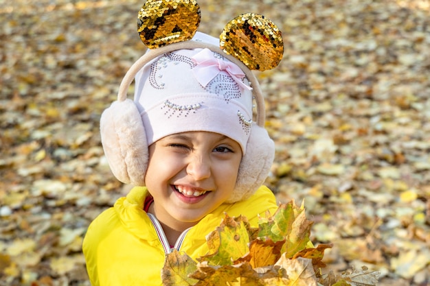 Mała słodka dziewczynka z bukietem żółtych opadłych liści jesienią w parku