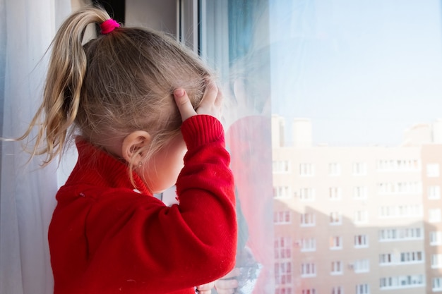 Mała Smutna Dziewczyna Patrzeje Przez Okno. Pozostań W Kwarantannie Domowej. Koncepcja Izolacji. Epidemia Wirusowa, Kryzys Medyczny