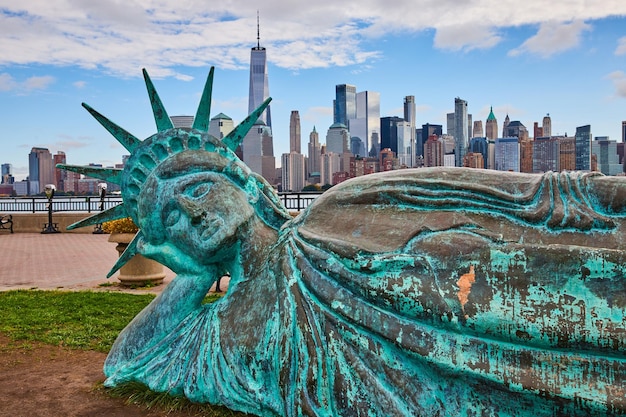 Mała statua wolności leżąca zardzewiała w New Jersey, z panoramą Nowego Jorku za nią