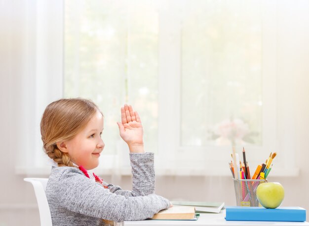 Mała studencka dziewczyna siedzi przy stołem i ciągnie jego rękę up.