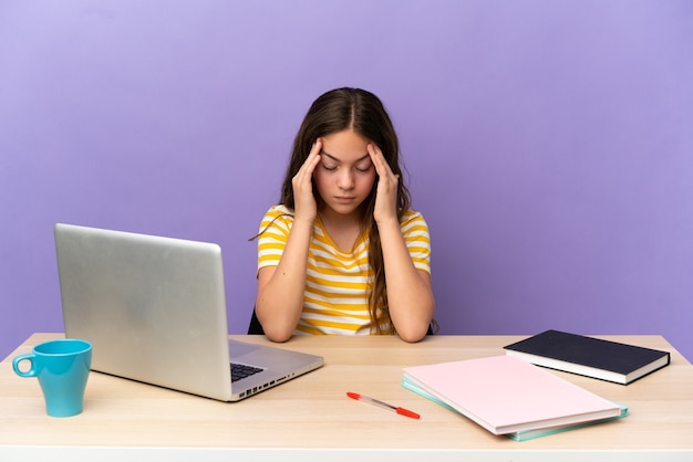 Mała studentka w miejscu pracy z laptopem na fioletowym tle z bólem głowy