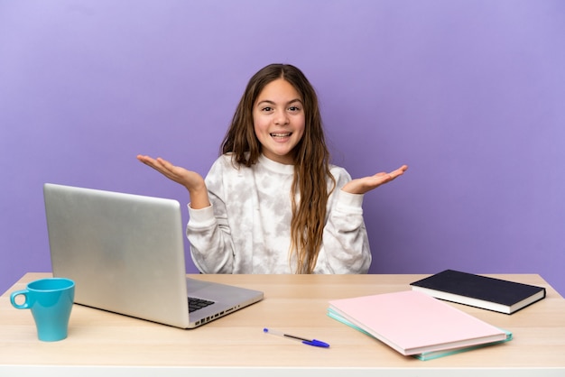 Mała studentka w miejscu pracy z laptopem na fioletowym tle ze zszokowanym wyrazem twarzy