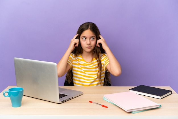 Mała studentka w miejscu pracy z laptopem odizolowanym na fioletowym tle, mająca wątpliwości i myśląca