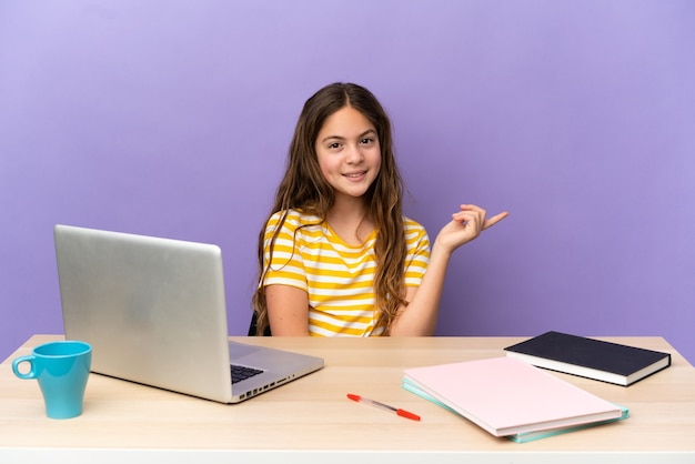 Mała studentka w miejscu pracy z laptopem odizolowanym na fioletowym tle szczęśliwa i skierowana w górę