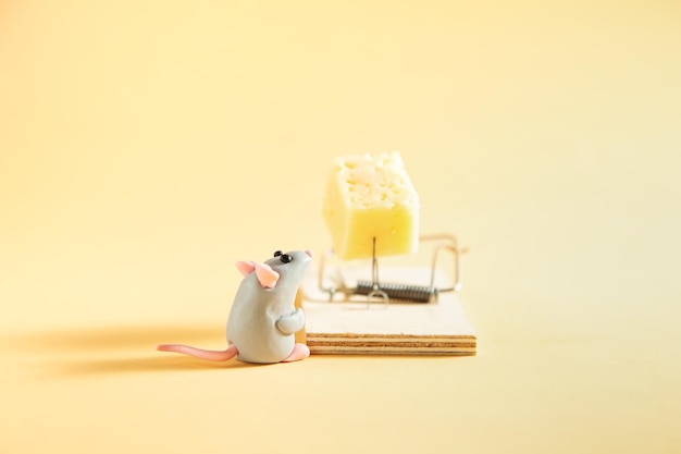 Mała szara mysz z plasteliny patrzy na kawałek sera w pułapce na myszy