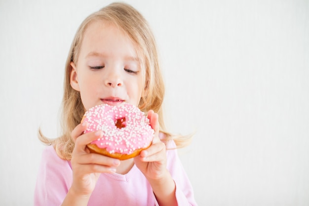 Mała Szczęśliwa Dziewczyna O Blond Włosach Bawi Się I Degustuje Pączki Z Różowym Lukrem Podczas Obchodów Chanuka