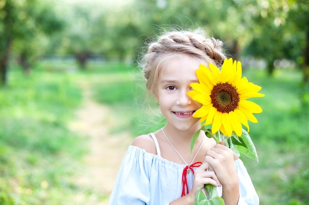 mała szczęśliwa dziewczynka uśmiecha się i zakrywa twarz słonecznikiem dziecko bawi się słonecznikiem