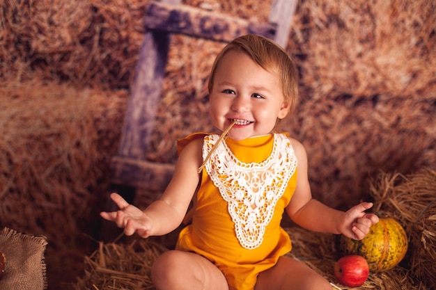 Mała szczęśliwa uśmiechnięta dziewczynka w wiosce siedzi na sianie ze zbiorami warzyw