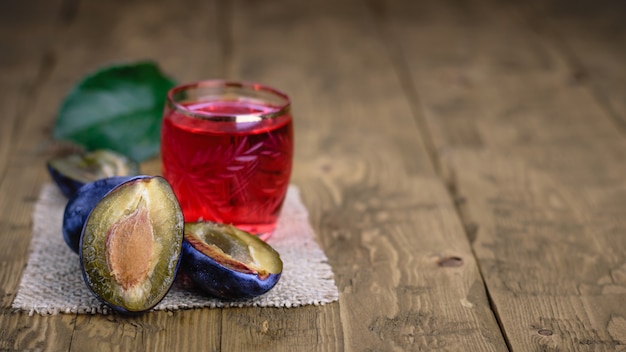 Mała szklanka domowego alkoholu ze śliwek jagodowych na drewnianym stole.