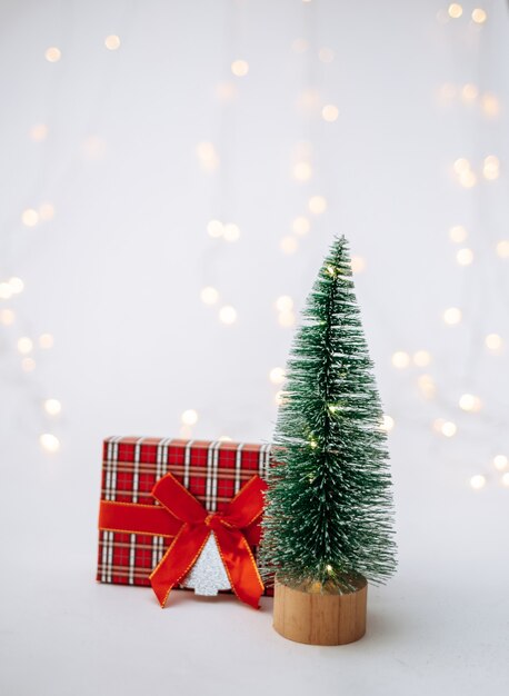 Mała sztuczna choinka z prezentem noworocznym na białym tle z bokeh z miejscem na tekst