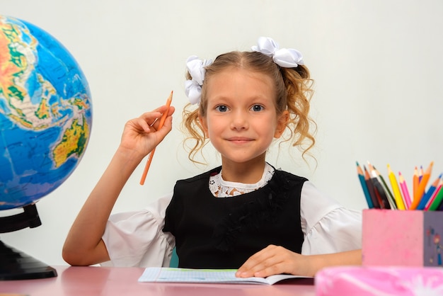 mała uczennica siedzi przy stole i uczy się na odosobnionym białym tle S