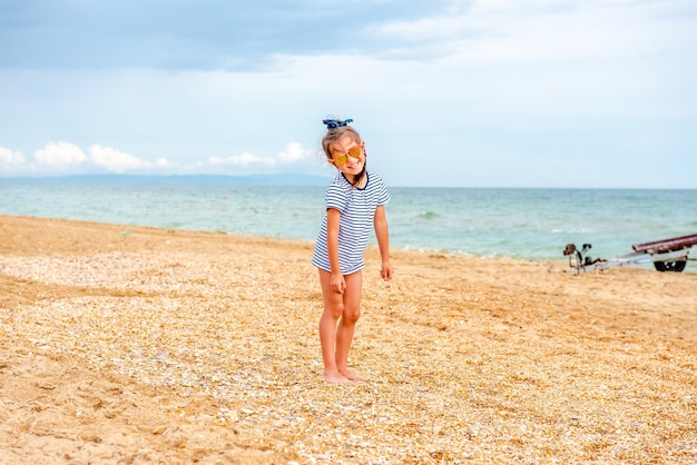 mała urocza dziewczynka w pasiastym t-shircie radośnie bawi się na plaży w słoneczny dzień na wakacjach