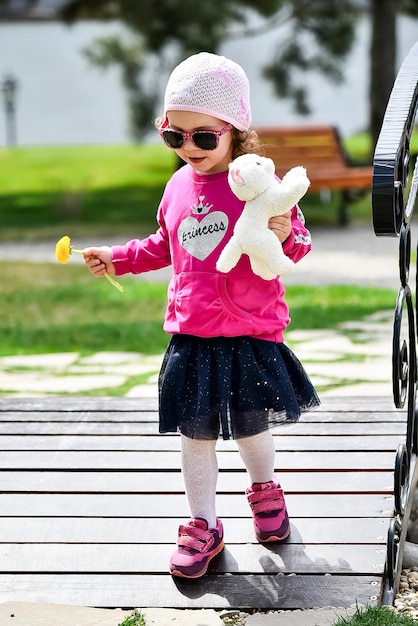 Mała urocza dziewczynka w różowej kurtce i różowym kapeluszu spaceruje po mieście Wiosna Słoneczne Szczęśliwe dzieciństwo