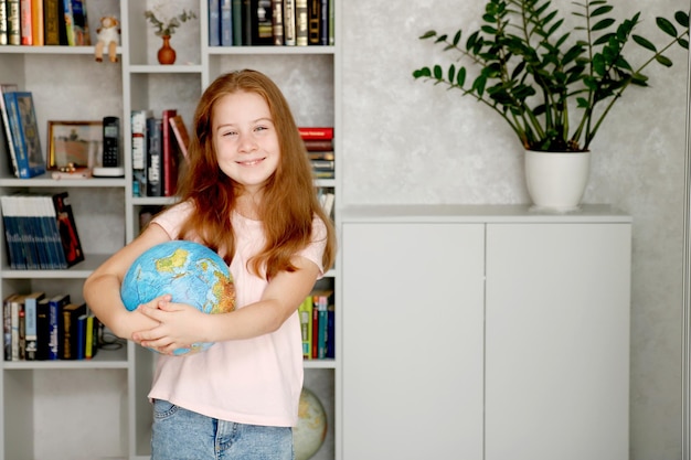 Mała uśmiechnięta dziewczyna trzymająca glob na tle półki z książkami