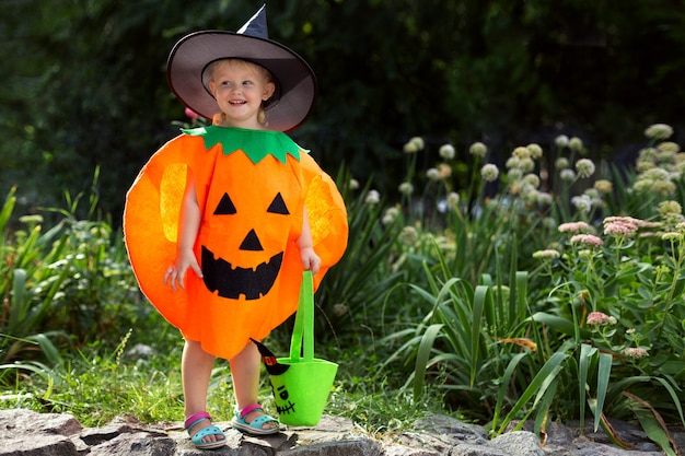 Mała Uśmiechnięta Dziewczynka W Dyniowym Kostiumie I Z Torbą Na Słodycze świętuje Halloween