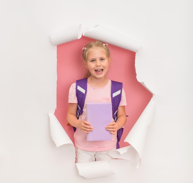 Mała uśmiechnięta dziewczynka ze szkolnym plecakiem i książką Powrót do koncepcji szkoły
