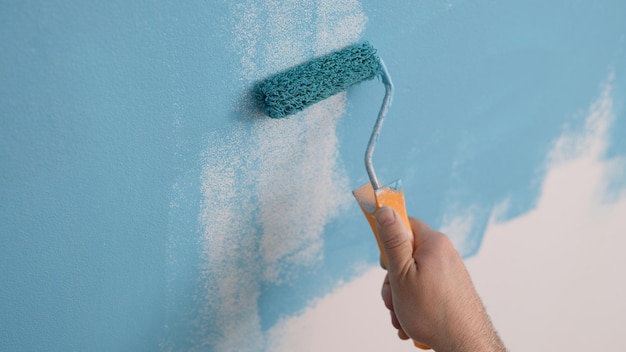 Malarz maluje ścianę na kolor niebieski za pomocą majsterkowania w domu i renowacji domu dekoracyjnego